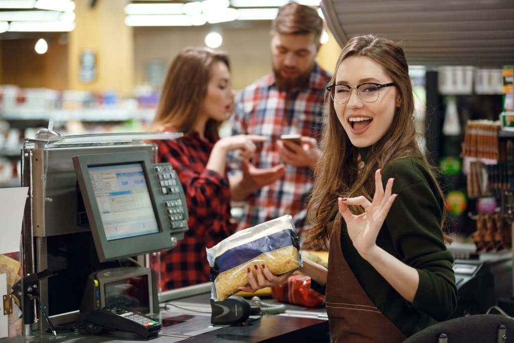 Kassiererin an einer Supermarktkasse, dahinter wartende Kundschaft